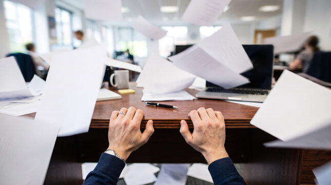 Frustrated office worker hands on desk with flying papers