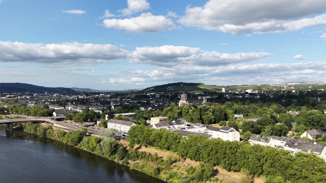 Drone aerial panorama of Trier, Germany, featuring hillside vineyards, the Moselle River, riverside woodland, a navigation lock and residential neighborhoods. Scenic summer landscape with rolling hill