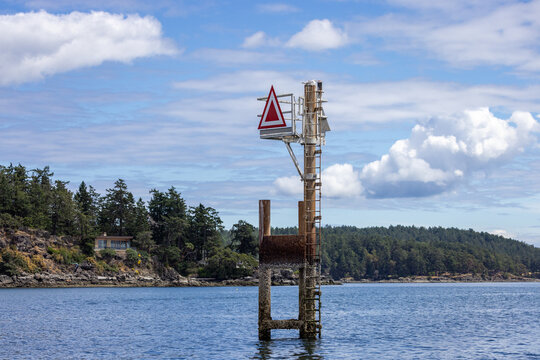 Red Triangle Navigation Marker On Wooden Pile Near Rocky Coastline Of Sidney, Vancouver Island, British Columbia