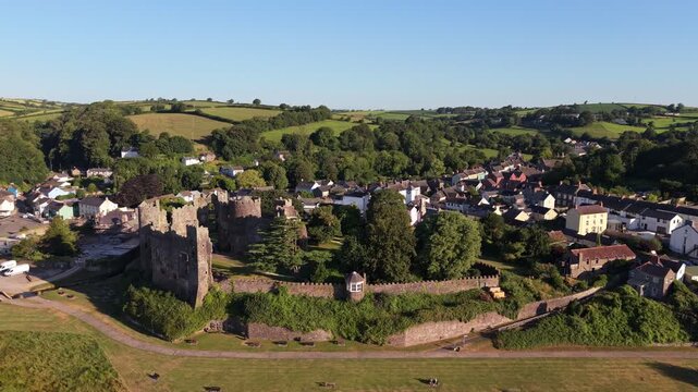 Aerial drone footage of the historic village of Laugharne in Carmarthenshire, Wales, featuring the River Coran estuary, traditional buildings, surrounding countryside and picturesque rural landscape 