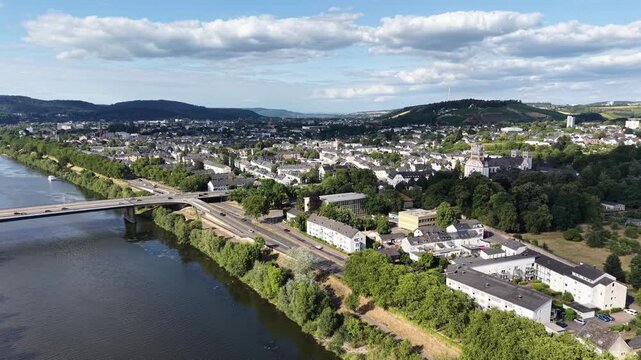 Drone aerial panorama of Trier, Germany, featuring hillside vineyards, the Moselle River, riverside woodland, a navigation lock and residential neighborhoods. Scenic summer landscape with rolling hill
