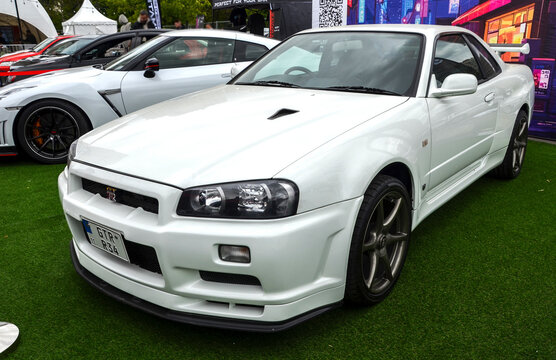 Legendary white Nissan Skyline GT-R R34 sports coupe, highlighting its clean body lines, aggressive front bumper, iconic grille badge, and dark custom wheels