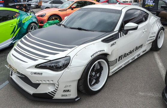 Heavily modified white Toyota GT86 featuring prominent Rocket Bunny widebody kit matte black hood with silver accent stripes tinted headlights and deep dish custom wheels