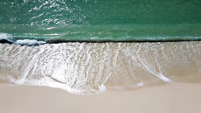 Top down aerial view of ocean waves crashing on a sandy beach