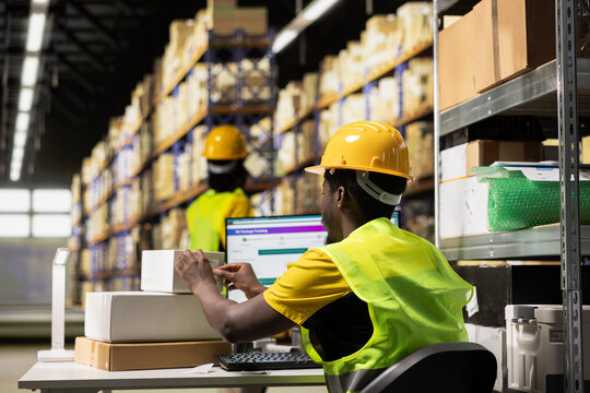 A Black warehouse clerk applies adhesive airway bill labels on boxes, preparing the merchandise for distribution with shipment details and other tracking info.