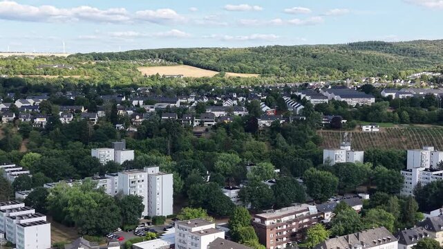 Drone aerial panorama of Trier, Germany, featuring hillside vineyards, the Moselle River, riverside woodland, a navigation lock and residential neighborhoods. Scenic summer landscape with rolling hill
