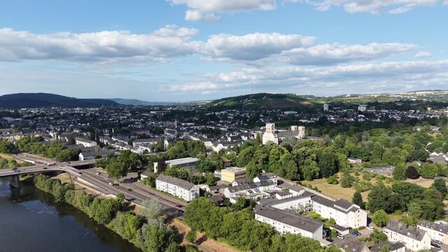 Drone aerial panorama of Trier, Germany, featuring hillside vineyards, the Moselle River, riverside woodland, a navigation lock and residential neighborhoods. Scenic summer landscape with rolling hill