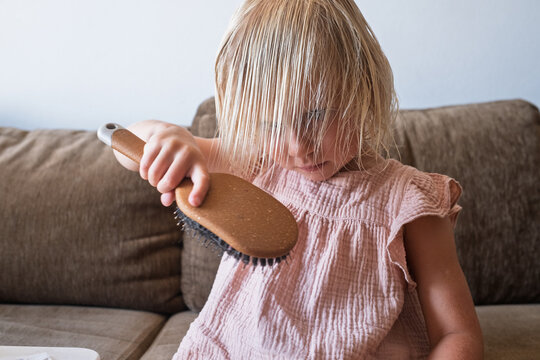  girl in a pink dress brushing her damp hair on a brown couch.