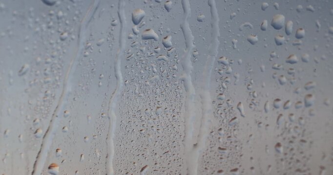 Small drops on the wet orange glass, drops of clear water cover the surface of the window due to the temperature difference outside and rain