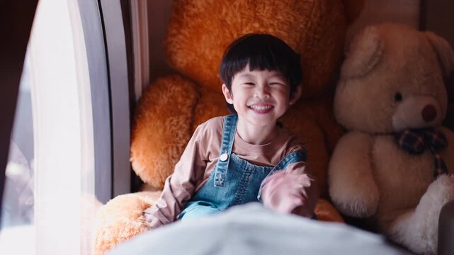 Happy young boy smiling and waving among giant teddy bears at home