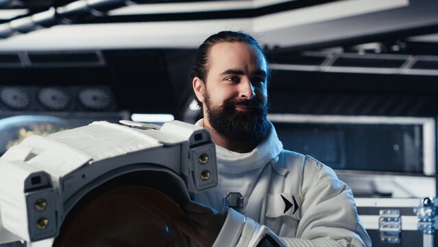 Smiling astronaut holds a helmet inside a space station while preparing for an exterior planetary mission and the start of landing procedures.