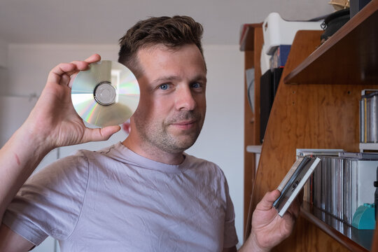 Man holding a compact disc near a bookshelf. 