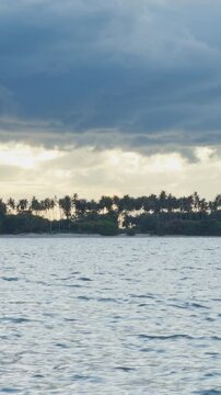 Vertical video. Slow Motion View of a Tropical Island Across Calm Water Beneath Dramatic Storm Clouds, Palm Trees, Rainfall, Coastal Scenery and Untamed Nature