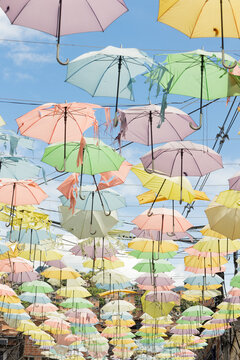 Numerous multicolored umbrellas hanging above a street. Their vibrant colors stand out against the blue sky, creating a decorative scene full of dynamism and visual appeal