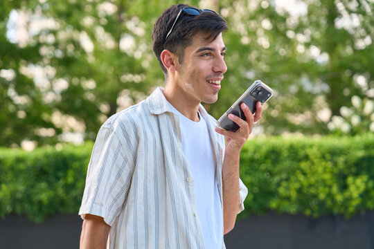 Young man using smartphone sending voice message outdoors