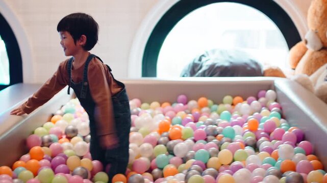 Energetic young boy leaping into a colorful indoor ball pit at a playground