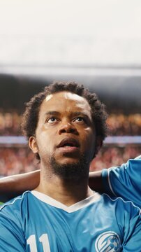 Vertical video: Portrait of diverse football players in blue jersey listening to national anthem during pre-match ceremony, match day opening on pitch with team in lineup, for football match content.