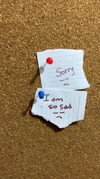 Close up of a hand attaching a handwritten notes onto a cork bulletin board .A symbol of apology and expressing feelings in simple notes