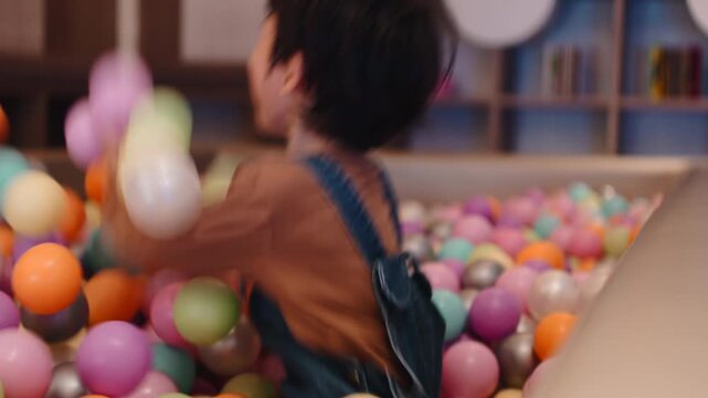 Young boy laughing and playing with his mother in a colorful ball pit