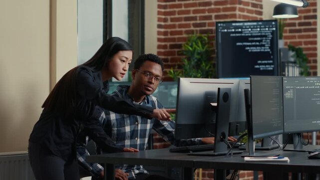 Two software developers carry a laptop with coding interface toward a development desk, preparing for software teamwork and project collaboration, while preparing code review.