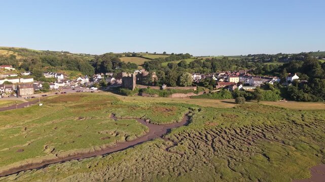 Aerial drone footage of the historic village of Laugharne in Carmarthenshire, Wales, featuring the River Coran estuary, traditional buildings, surrounding countryside and picturesque rural landscape 