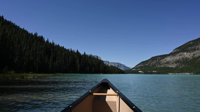 POV from a canoe while paddling on a mountain lake with a clear blue sky. Includes the sound of the paddle in the water