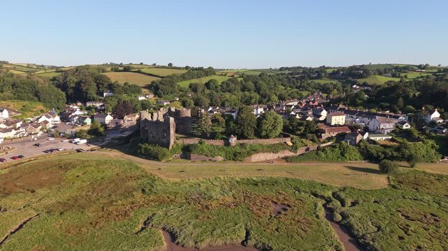 Aerial drone footage of the historic village of Laugharne in Carmarthenshire, Wales, featuring the River Coran estuary, traditional buildings, surrounding countryside and picturesque rural landscape 