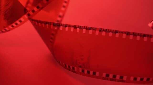 35mm negative photographic film in rotation in red room, camera darkroom. Slightly rolled film strip isolated on red background. Analog film strips. Analog photography. Close-up