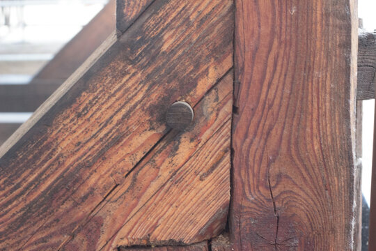 Close-up of weathered reddish-brown wooden beams joined together with a traditional round wooden peg or dowel, showcasing detailed natural grain and rustic craftsmanship.