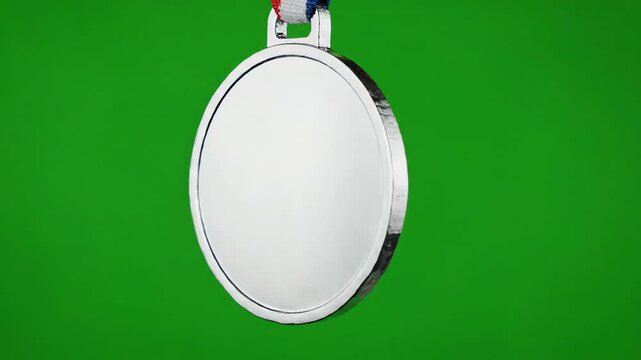 Blank shiny silver medal spinning slowly on a bright green screen background for chroma key compositing