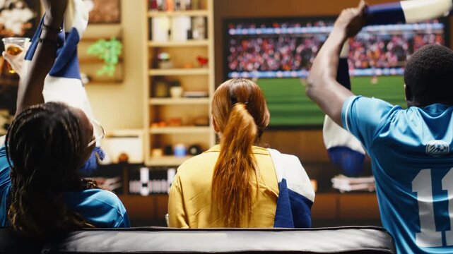 Tight framing shows happy soccer supporters excited by football game action on living room TV while football fans react with loud weekend match energy.