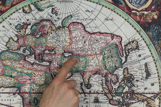 Close up to a male hand pointing with his index finger to the asian continent into a modern printed reproduction of a 1630 map