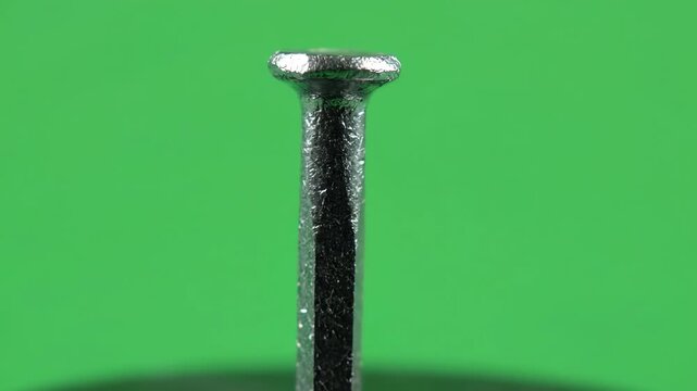 Close up macro shot of a metal horseshoe nail rotating slowly against a chroma key green screen background