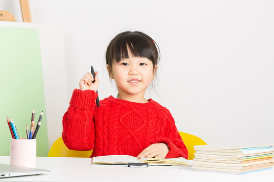 Intelligent Chinese girl doing homework at desk, thinking deeply and having a great idea or eureka moment.