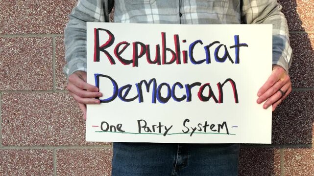 Demonstrator holds a handmade sign reading Republicrat Democran One Party System protesting corporate influence political duopoly elections and choice