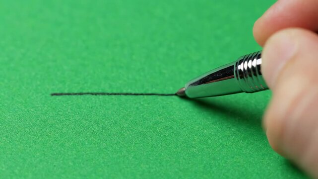 Close up view of a metallic ballpoint pen drawing a precise horizontal line on a chromakey green surface