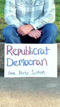 Demonstrator holds a handmade sign reading Republicrat Democran One Party System protesting corporate influence political duopoly elections and choice
