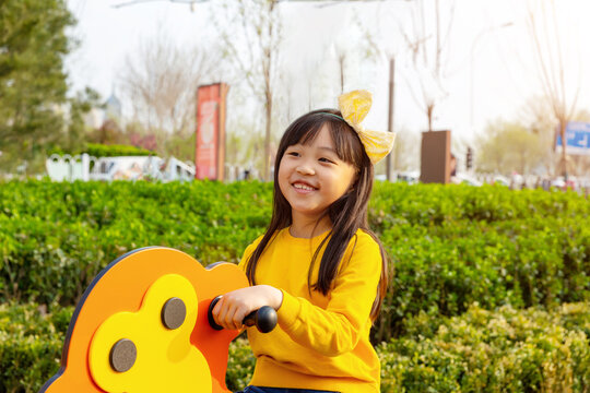 Cheerful little girl rides on a colorful spring rocker toy at a community playground in springtime.