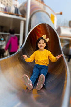 Excited little girl slides down a large outdoor tunnel slide with a bright smile on her face.