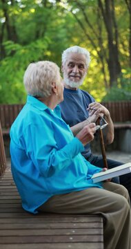 Elderly people spending time together on bench in park, camera moving