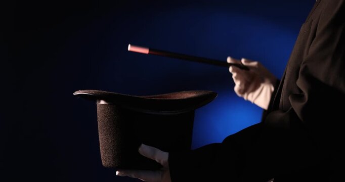 Magician showing trick with wand and top hat on stage, closeup