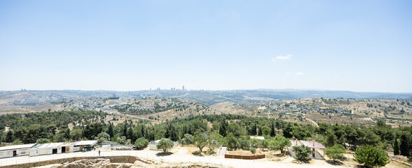 Obraz premium High-angle panoramic vista of rolling forested hills, distant urban settlements, and city skylines under a hazy blue sky.