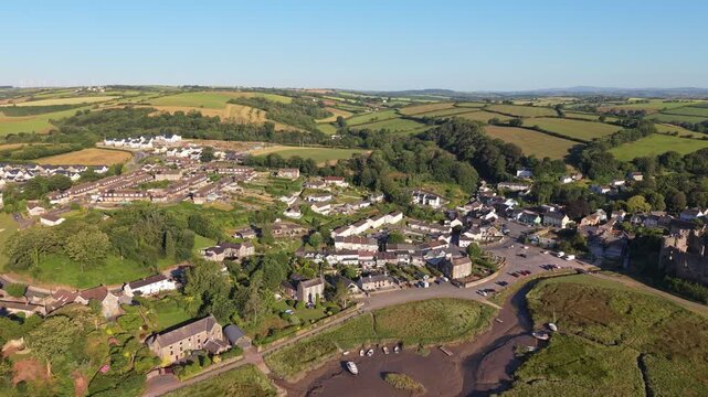 Aerial drone footage of the historic village of Laugharne in Carmarthenshire, Wales, featuring the River Coran estuary, traditional buildings, surrounding countryside and picturesque rural landscape 