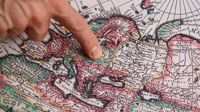 Detailed view of a male hand pointing with his index finger to the central europe region into a modern printed reproduction of a 17th century map