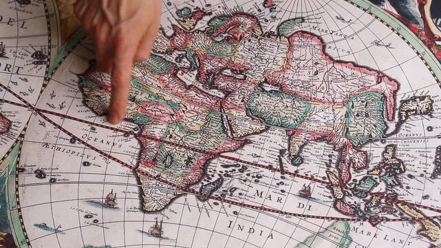Detailed view of a male hand pointing an antique spice route with his index finger from spain to India into a modern printed reproduction of a 17th century map