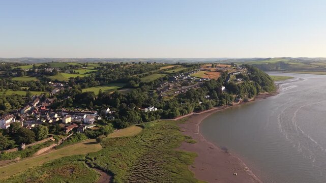 Aerial drone footage of the historic village of Laugharne in Carmarthenshire, Wales, featuring the River Coran estuary, traditional buildings, surrounding countryside and picturesque rural landscape 