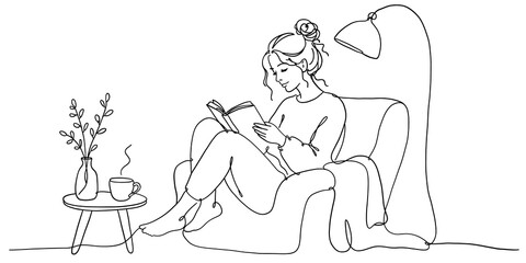 Young woman reading a book and relaxing in a cozy armchair at home