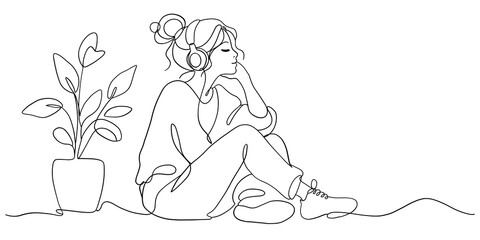 Young woman sitting and listening to music with headphones near indoor plant