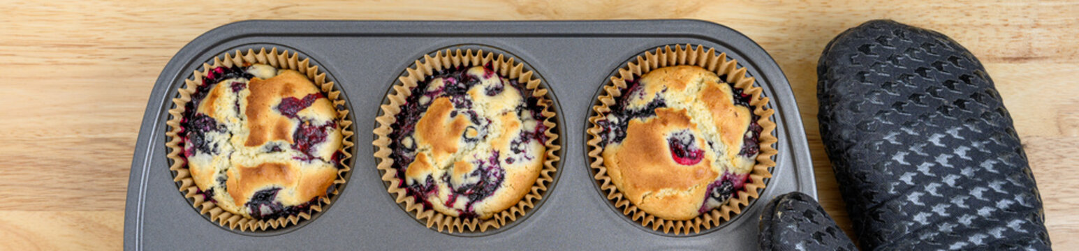 Fresh from the oven hot baked lemon blueberry muffing with golden top in jumbo muffin pan with paper liners, and oven mitts, on wood kitchen counter, baking tasty pastries at home
