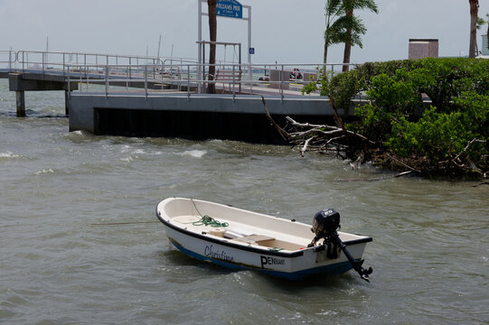 Small white motorboat moored near a concrete pier and mangrove shoreline, bobbing in choppy coastal water. Editorial Use Only July 21, 2026 Gulfport,FL USA. Under natural light; evokes solitude, leisu